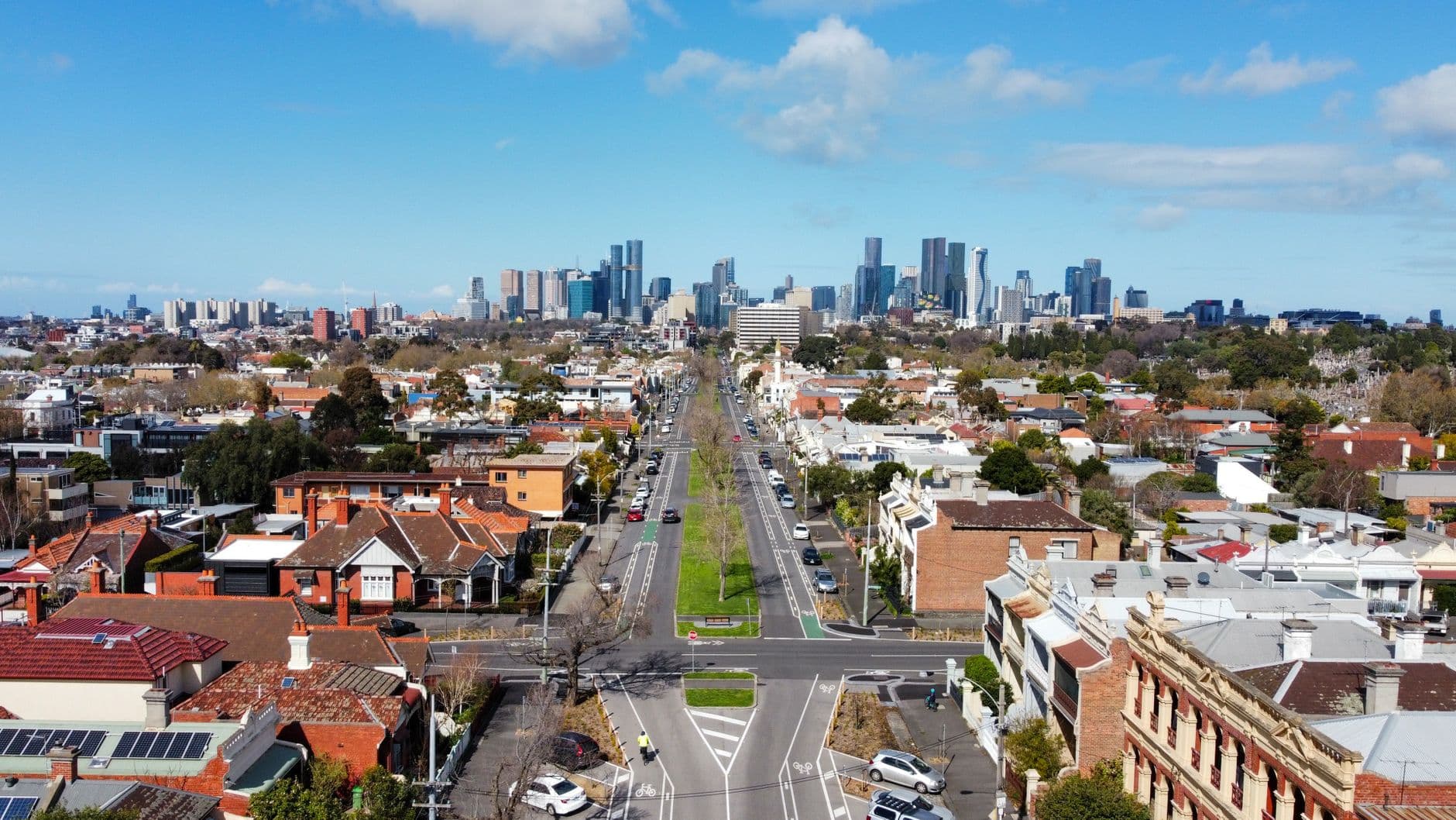 Aerial view of an inner Melbourne suburb with period homes and a tree-lined boulevard leading to the city skyline.